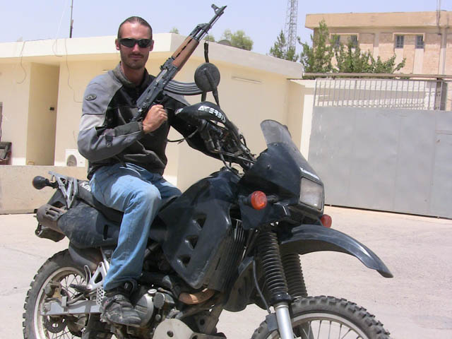 Matthew VanDyke with his Kawasaki KLR650 motorcycle and an AK-47 assault rifle in Iraq