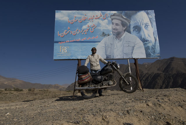 Matthew VanDyke with his MZ Kanuni motorcycle in front of a Ahmad Shah Massoud billboard in the Panjshir Valley of Afghanistan